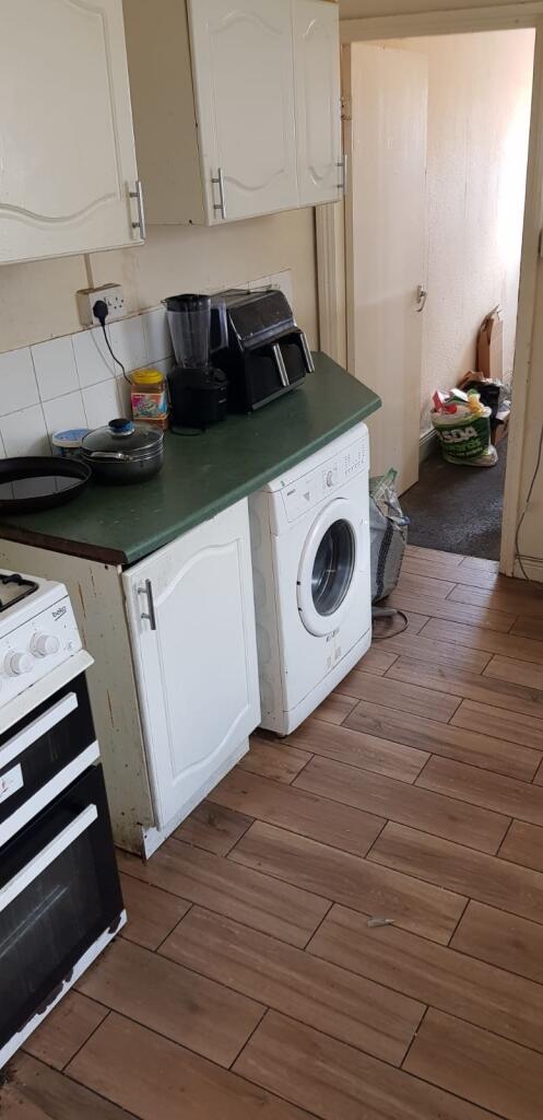 A compact kitchen featuring white cabinetry and...