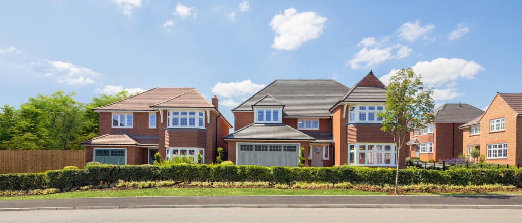 A row of modern detached houses with brick exteriors and well-maintained gardens under a blue sky wi