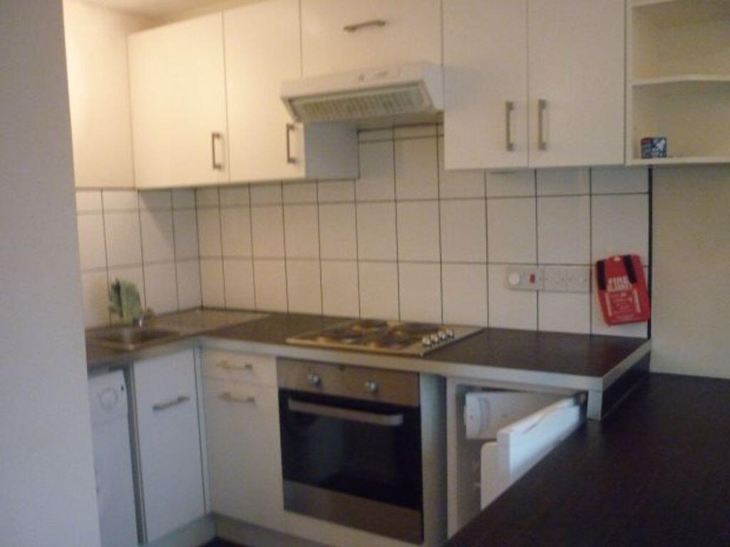 A compact kitchen area featuring white cabinetr...