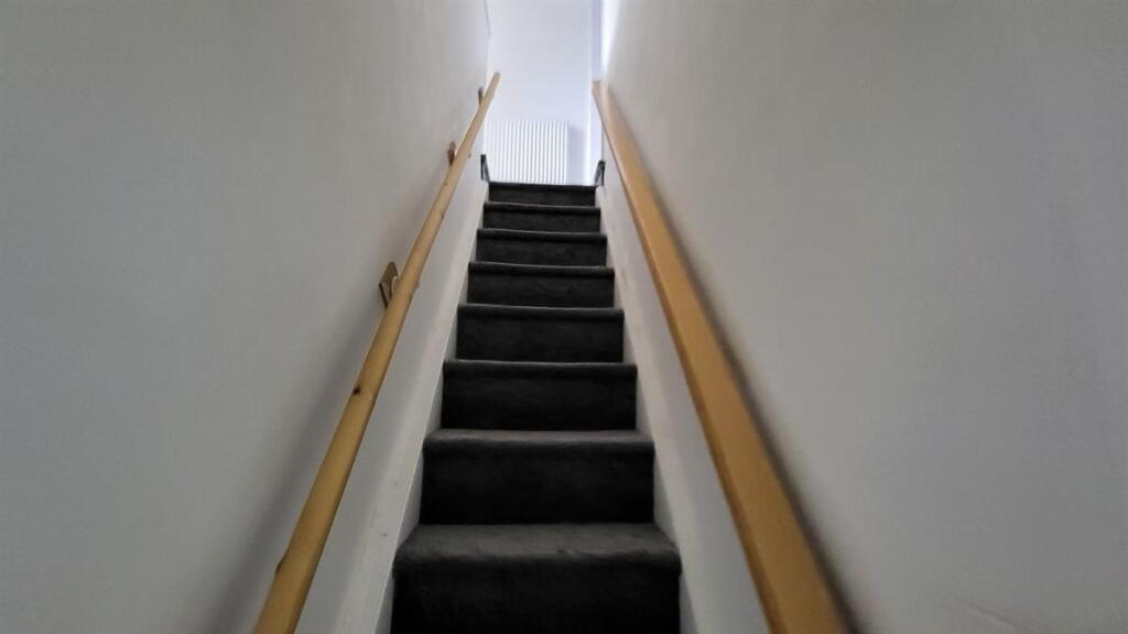Narrow carpeted staircase with light-colored wa...