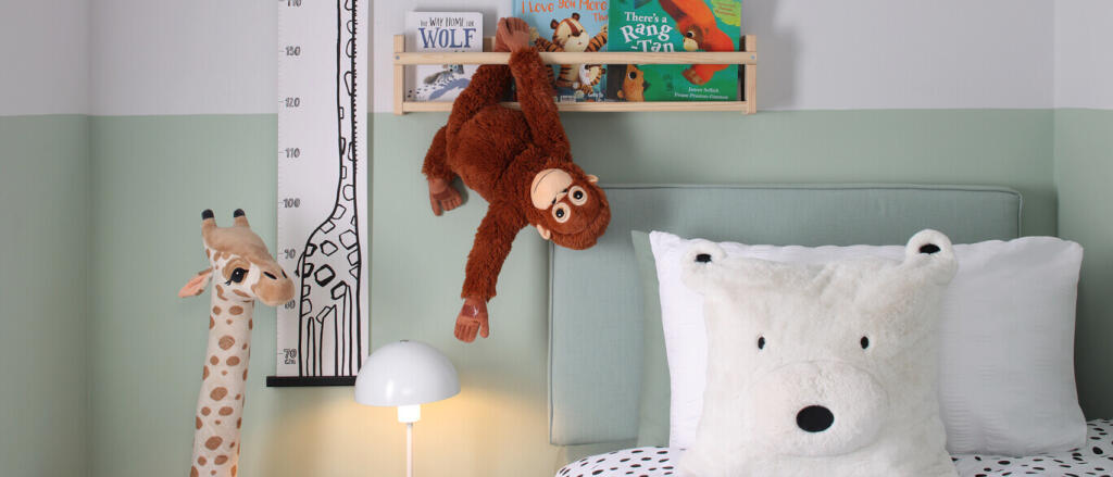 Children's bedroom with plush animal pillows, a hanging monkey toy, a giraffe lamp, children's books