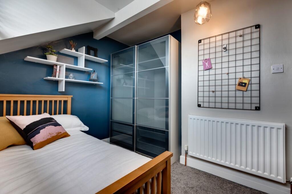 A cozy bedroom featuring a simple wooden bed fr...