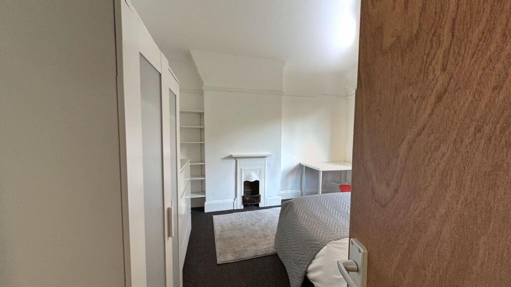 A cozy bedroom featuring a small fireplace, a w...