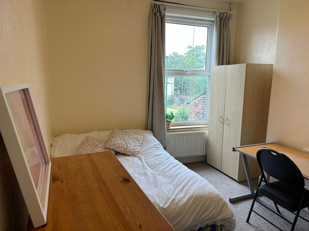 A cozy, well-lit room featuring a single bed wi...