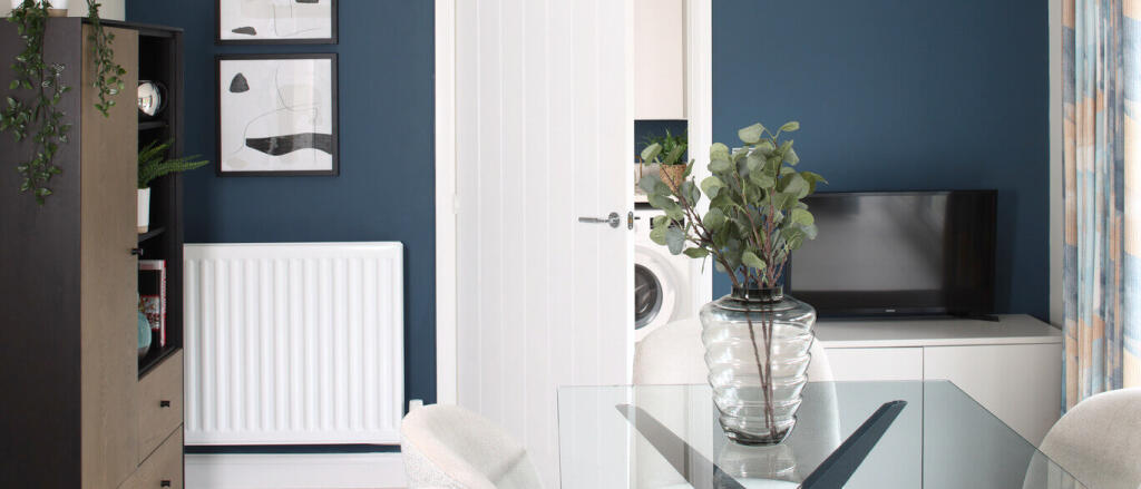 Modern living room with blue accent wall, white radiator, glass dining table, and a TV with colourfu