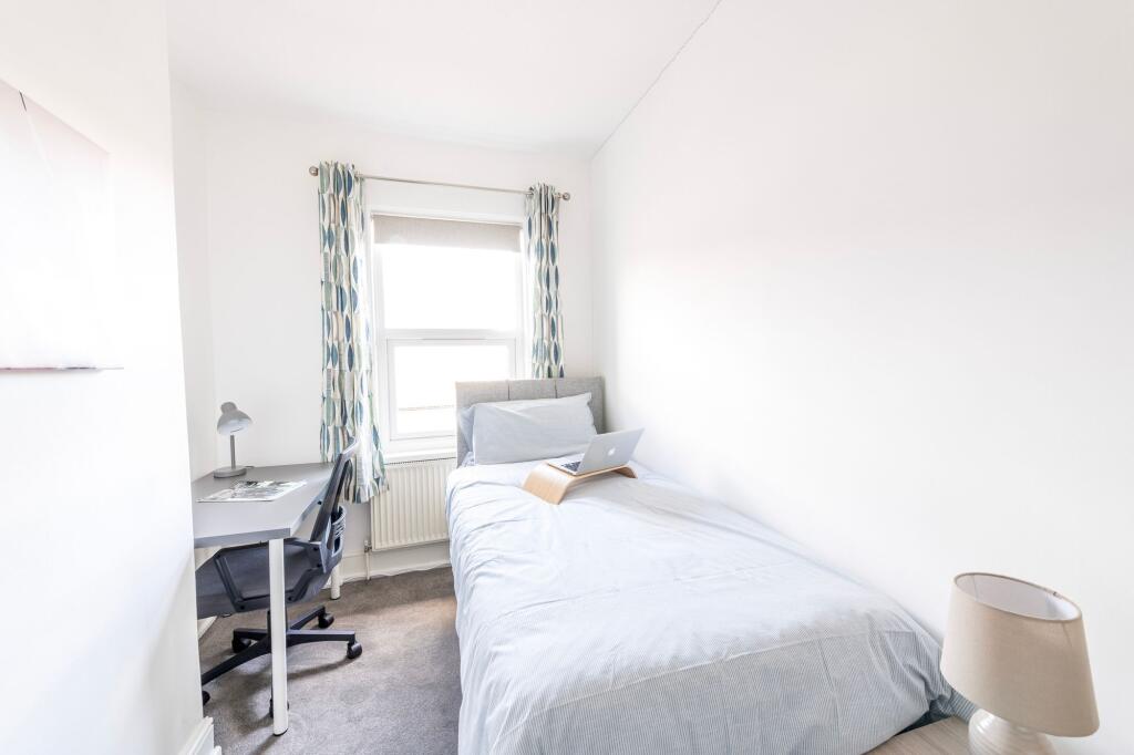 A bright, minimalist single bedroom featuring a...