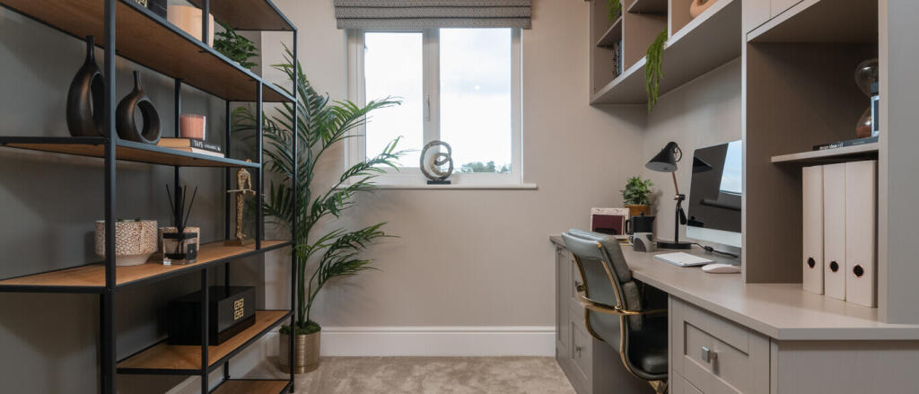 A home office with a grey desk and chair, a window with a view, and decorative items including plant