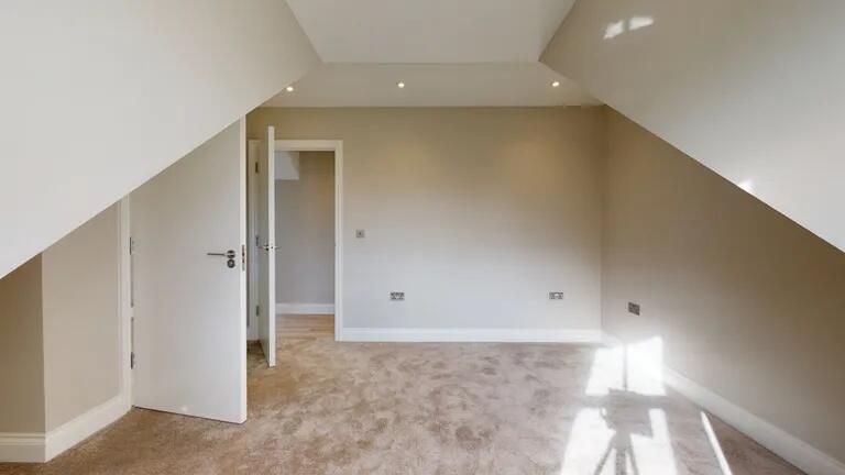 Bright attic room with beige walls and carpet f...