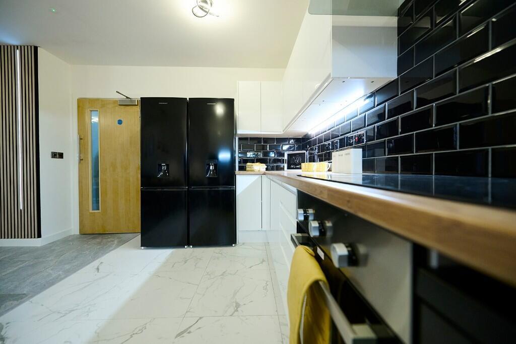 A modern kitchen featuring sleek black tiled ba...