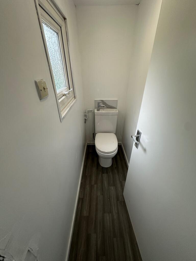 A narrow and clean single toilet with white wal...