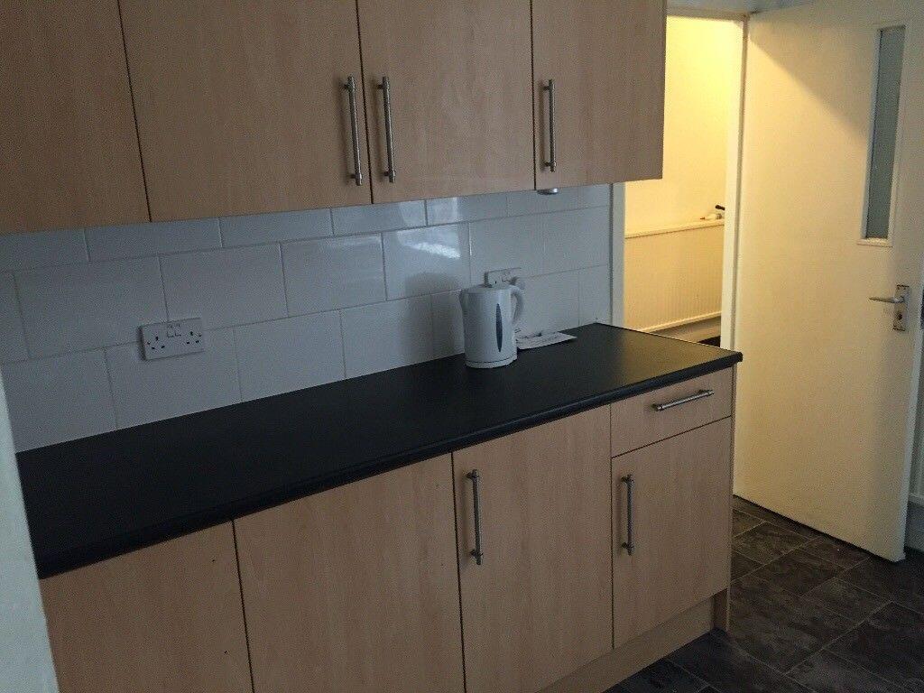 Compact kitchen with light wood cabinets, black...