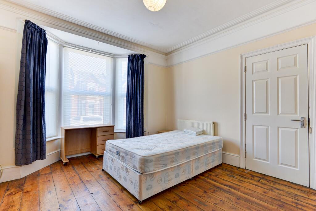 A bright single bedroom featuring a wooden floo...