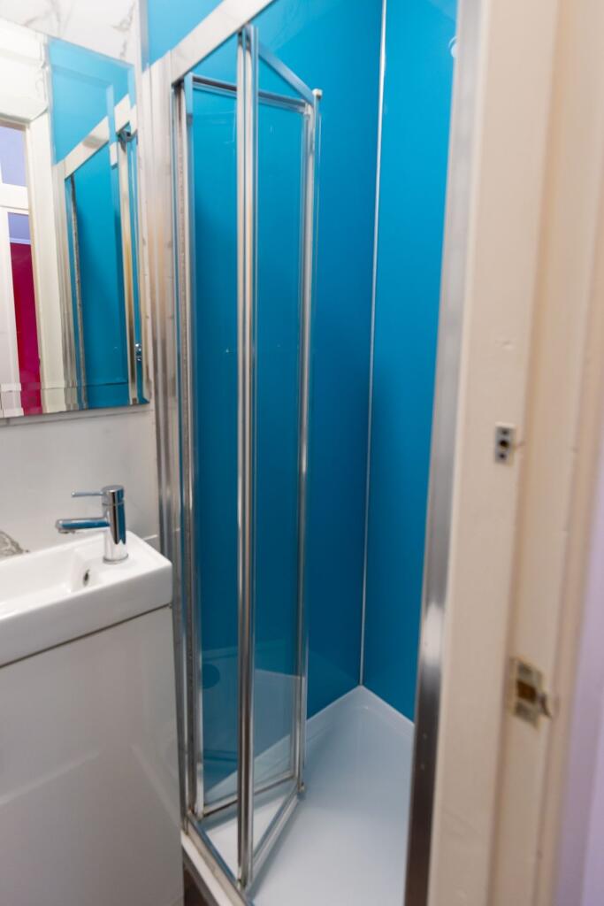 A compact bathroom featuring a blue shower encl...