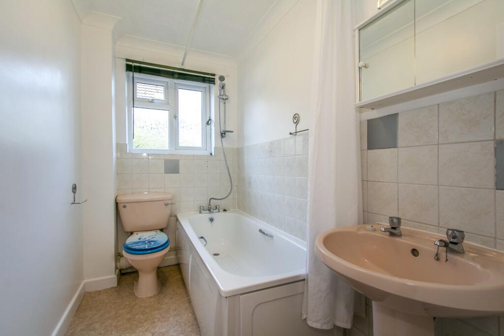 Bathroom with half tiled walls and lino flooring. The bathroom comprises a bath with a shower over the bath, wash basin and toilet.